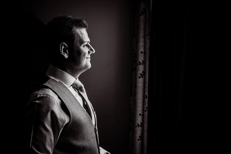 Black & White Portrait photo of The groom Jordan looking out of the window at Eastwell Manor, Kent