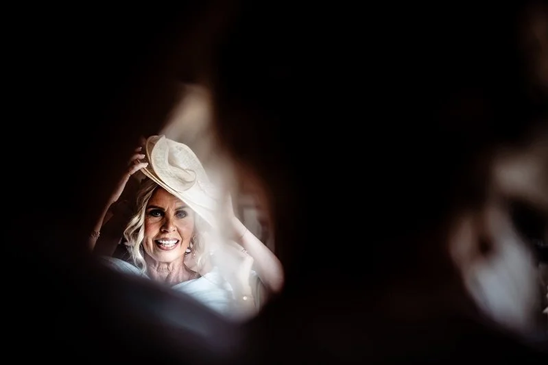 Colour photo of Mother of the bride putting her hat on in the mirrow