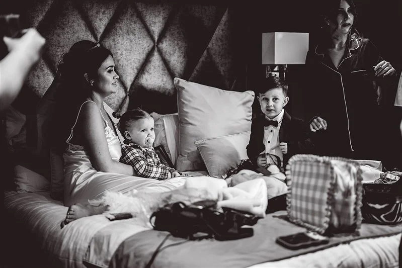 Black & White photo of the bride, flower girl & page boy sitting on the bed