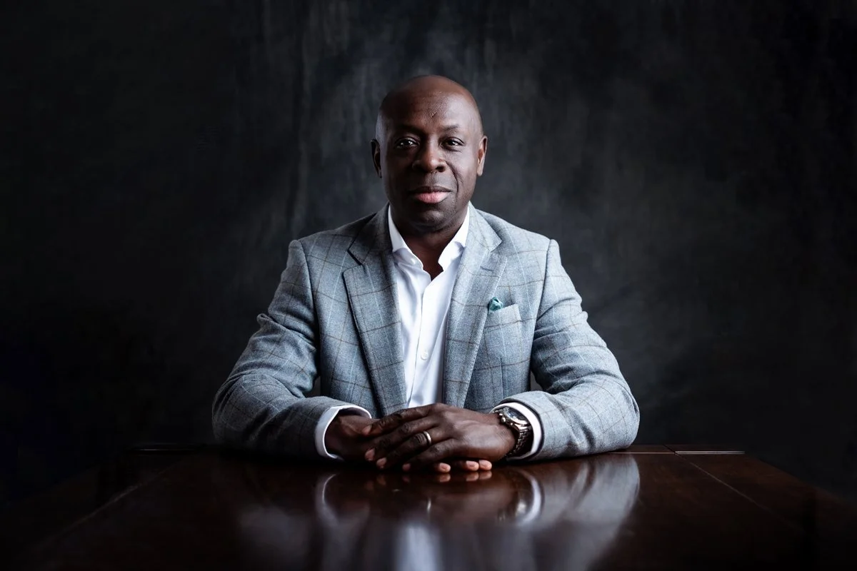 three quarter length portrait of a Black man wearing smart suit and white shirt with his hands on a table - London Portrait Photographer Matt Rock