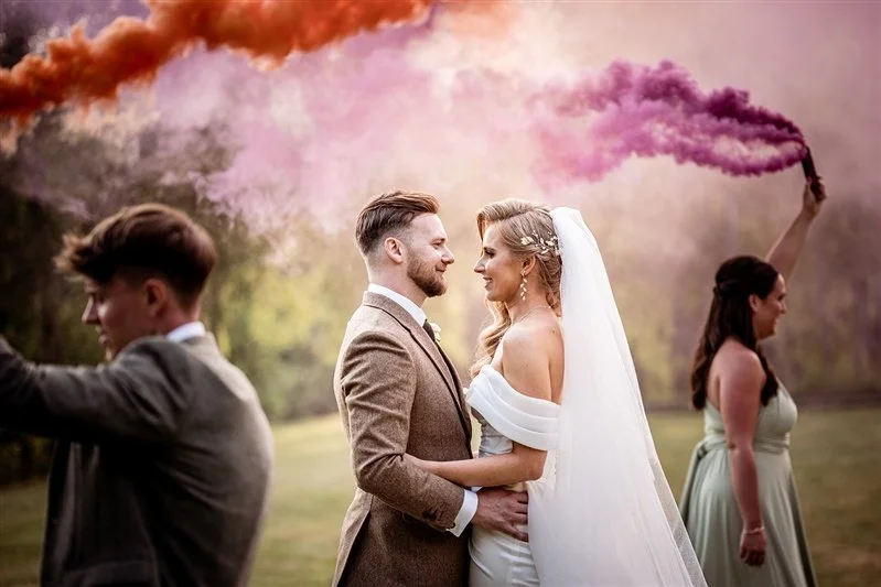 Colour photo of the bride and groom with smoke bombs being waved by the best man and bridesmaid. Wedding Photographer at Salomons Estate - Tonbridge Wells, in Kent