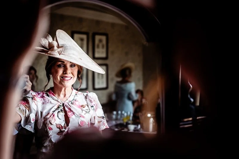 Mother of the groom getting her hat on in the mirrow before the wedding ceremony at Eastwell Manor