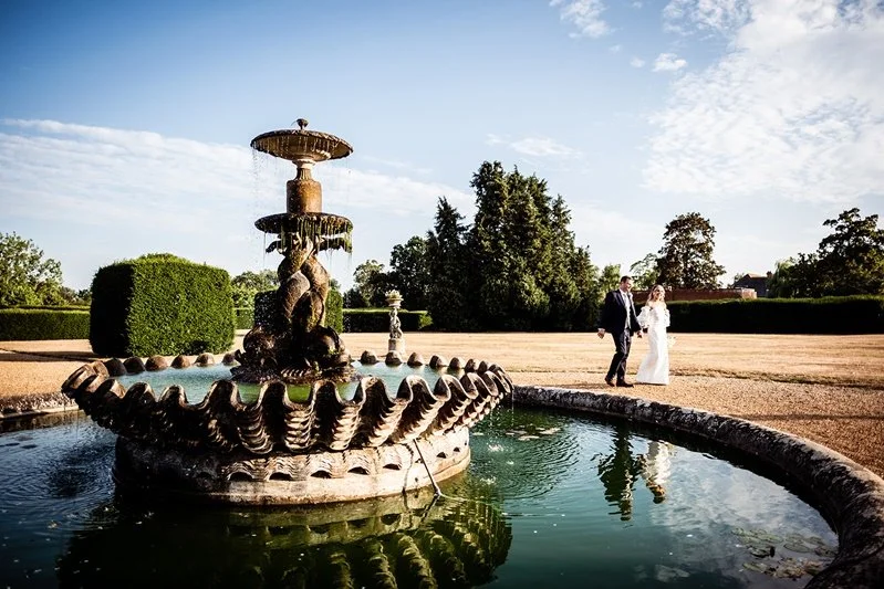 Colour photo of the bride and groom walking around the fountain at Eastwell Manor