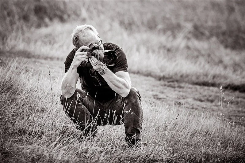 Portrait of Matt Rock working outside using a Nikon camera dressed in a t shirt and jeans