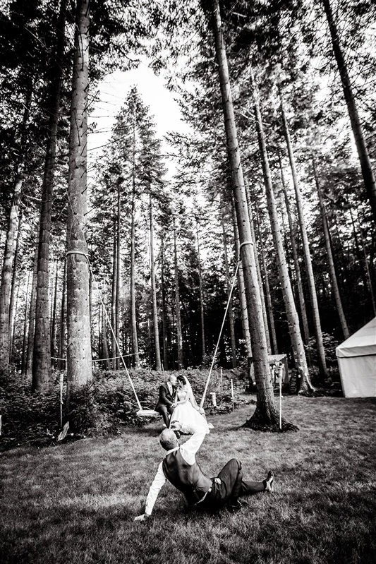 Black and white photo of Matt Rock taking a photo of the bride and groom on a swing at a wedding in Longton Woods Kent