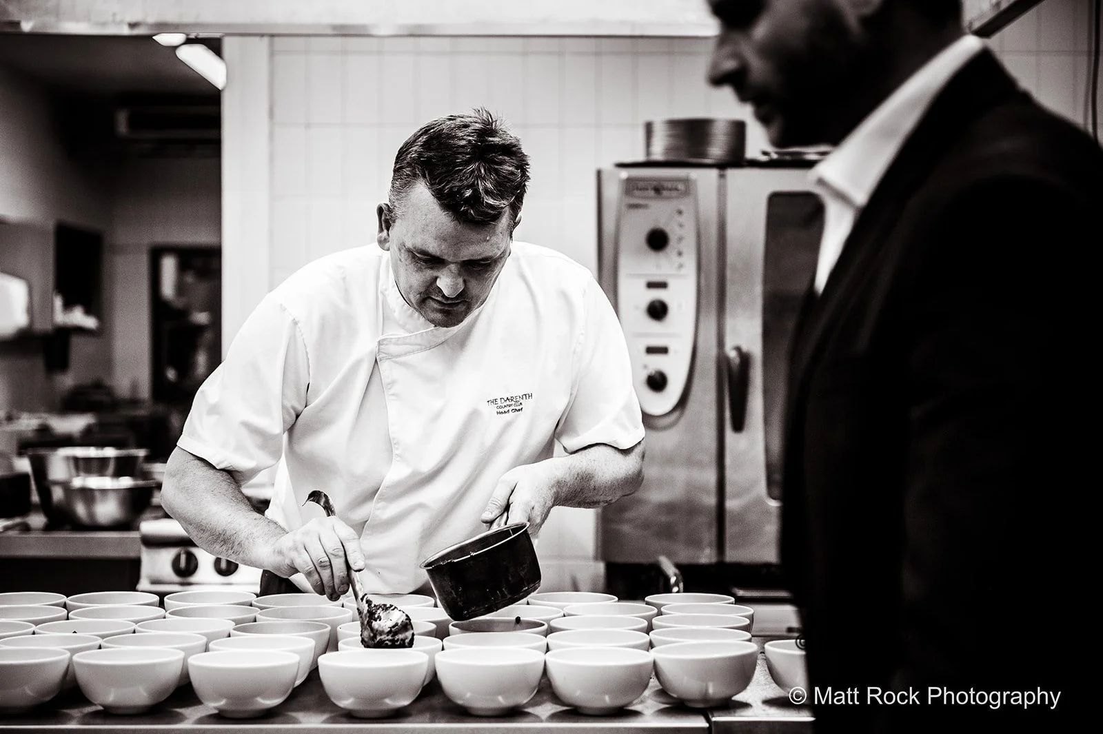 Black & White photo of a Commercial kitchen shoot in Kent of a chef and assistant making up the meals. 