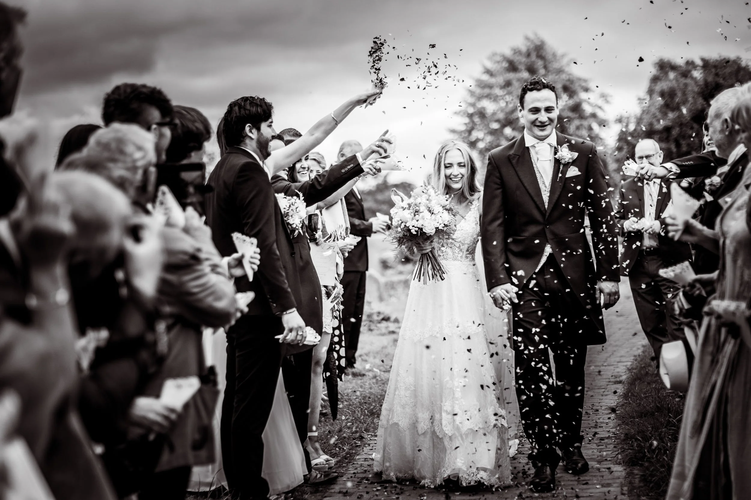 Black & white photo of the bride and groom walking through their gusts throwing confetti over them. Kent, Uk.