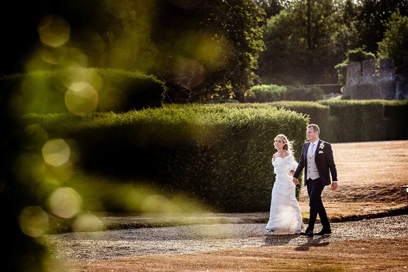 Colour photo of the bride and groom walking hand in hand in the grounds of Eastwell Manor, Ashford, Kent