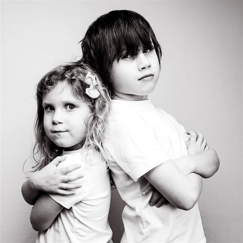 Black and white portrait of two children in a studio folding their arms