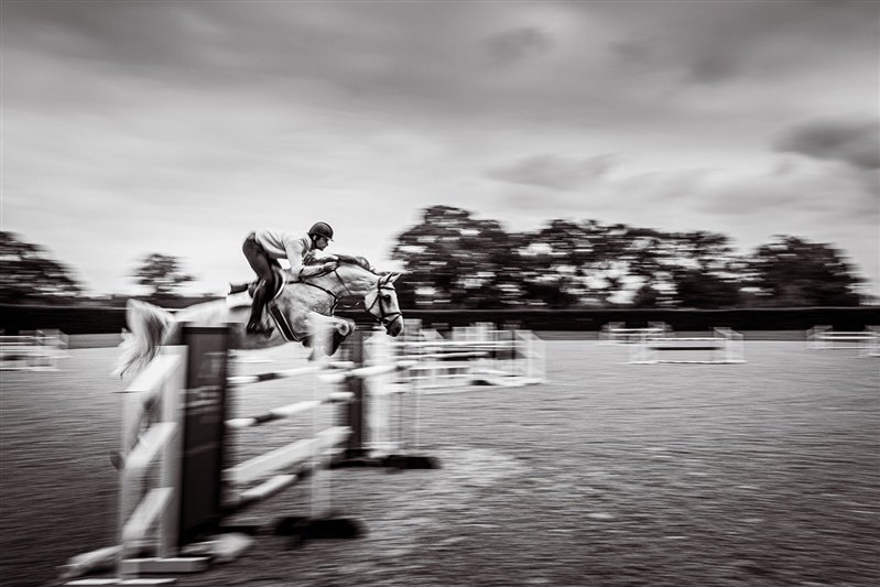 Black & white Commercial equestrian shoot - Rider and horse jumping in a stable - UK 