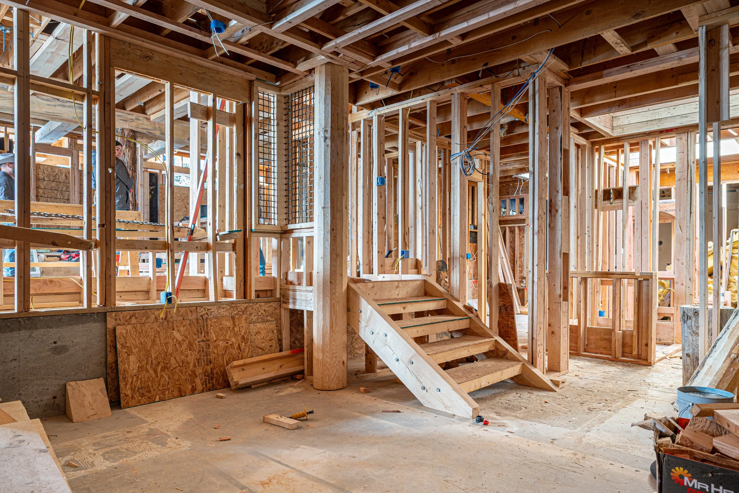 Interior view of a house under construction, showing wooden framing, stairs, and electrical wiring.