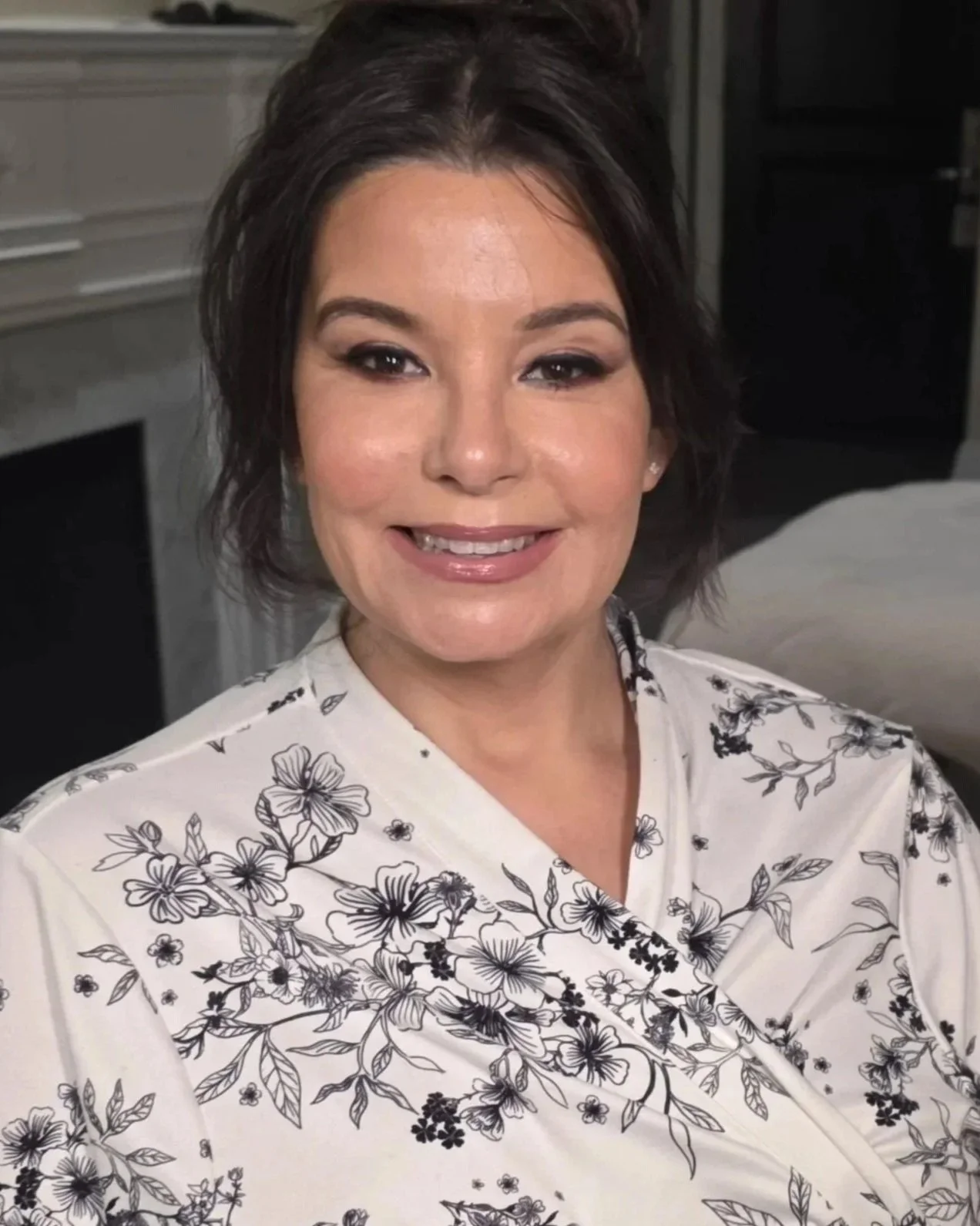 A woman with short dark hair smiling, wearing a white top with black floral print.