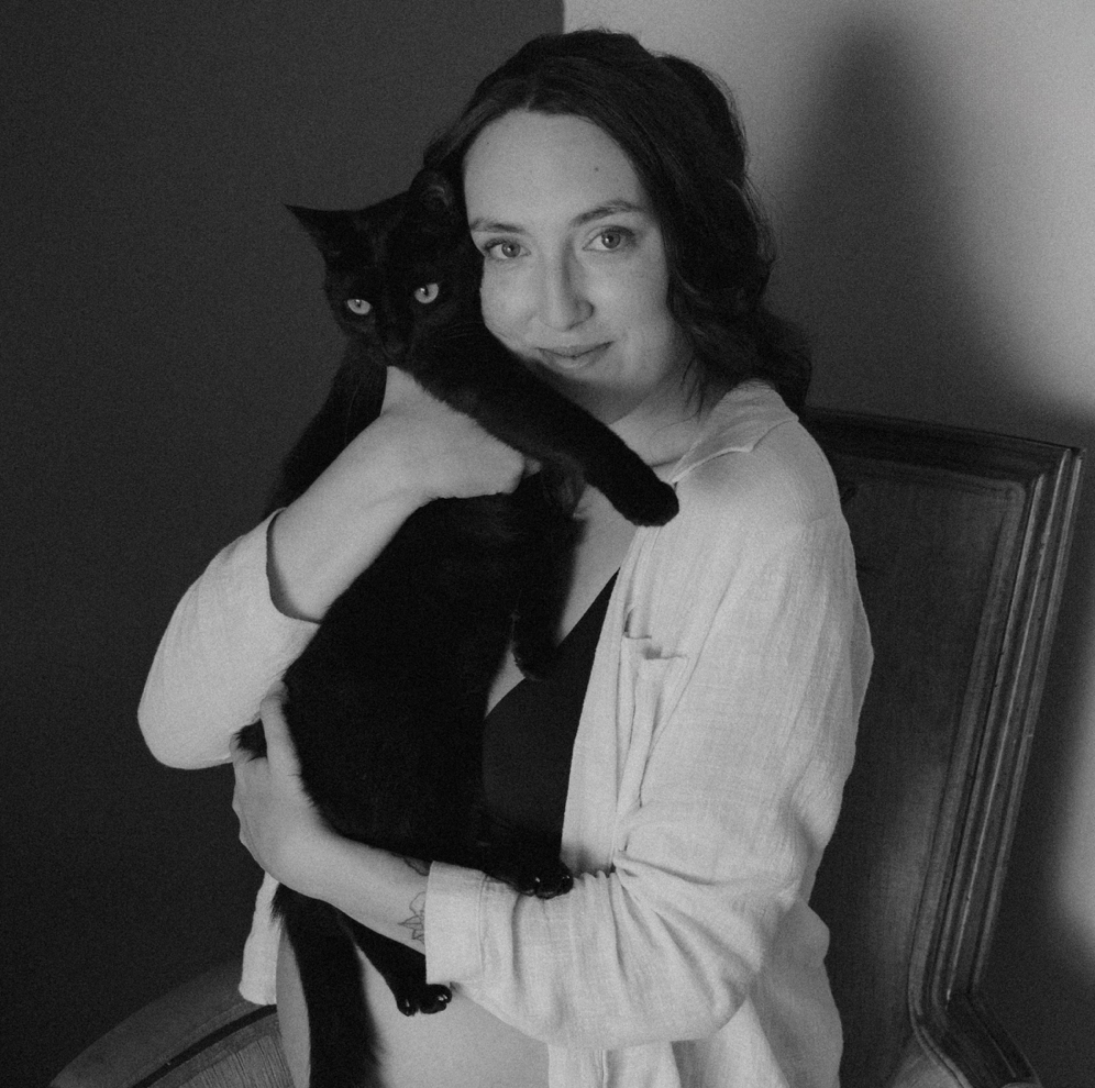 Black and white photo of a person holding a black cat on an armchair.