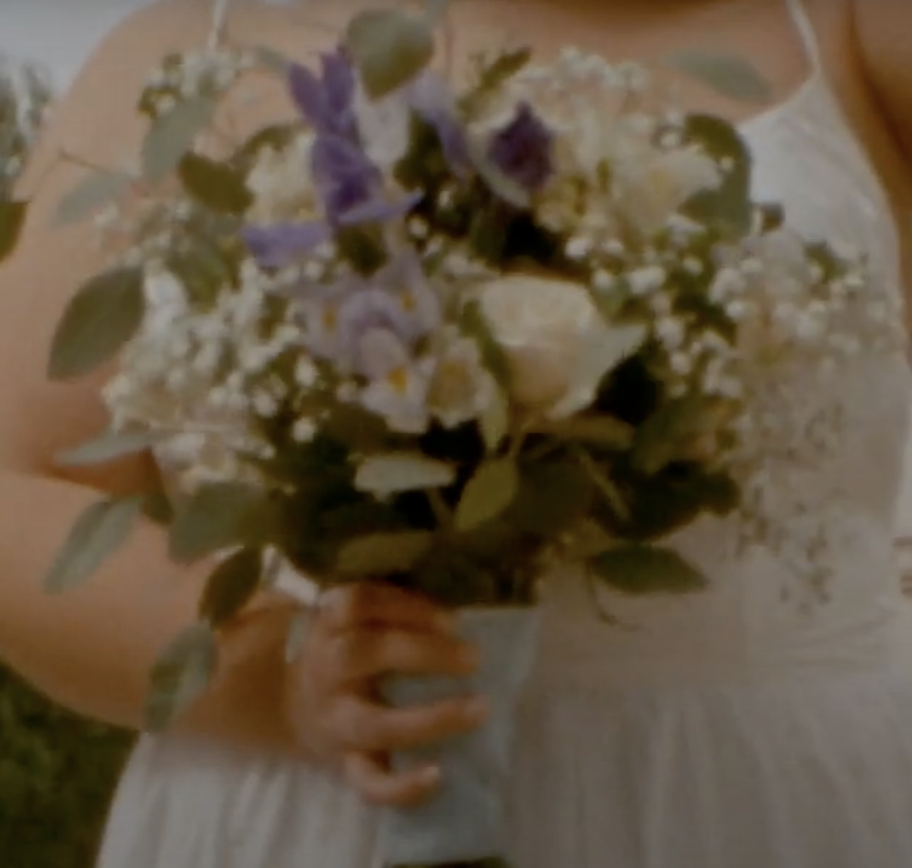 A person holding a bouquet of flowers and greenery on a wooden surface.