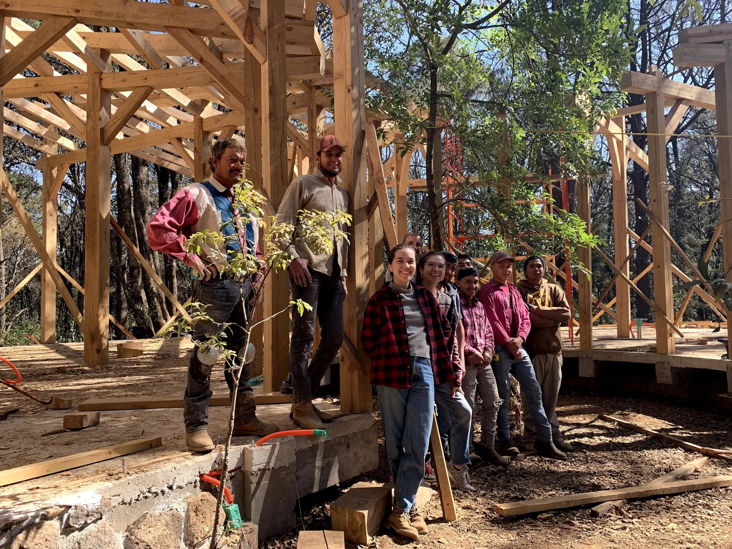 Equipo de Recinta sonriente frente a una estructura de madera en construcción en el bosque, como parte de un proyecto de bioconstrucción y arquitectura sustentable
