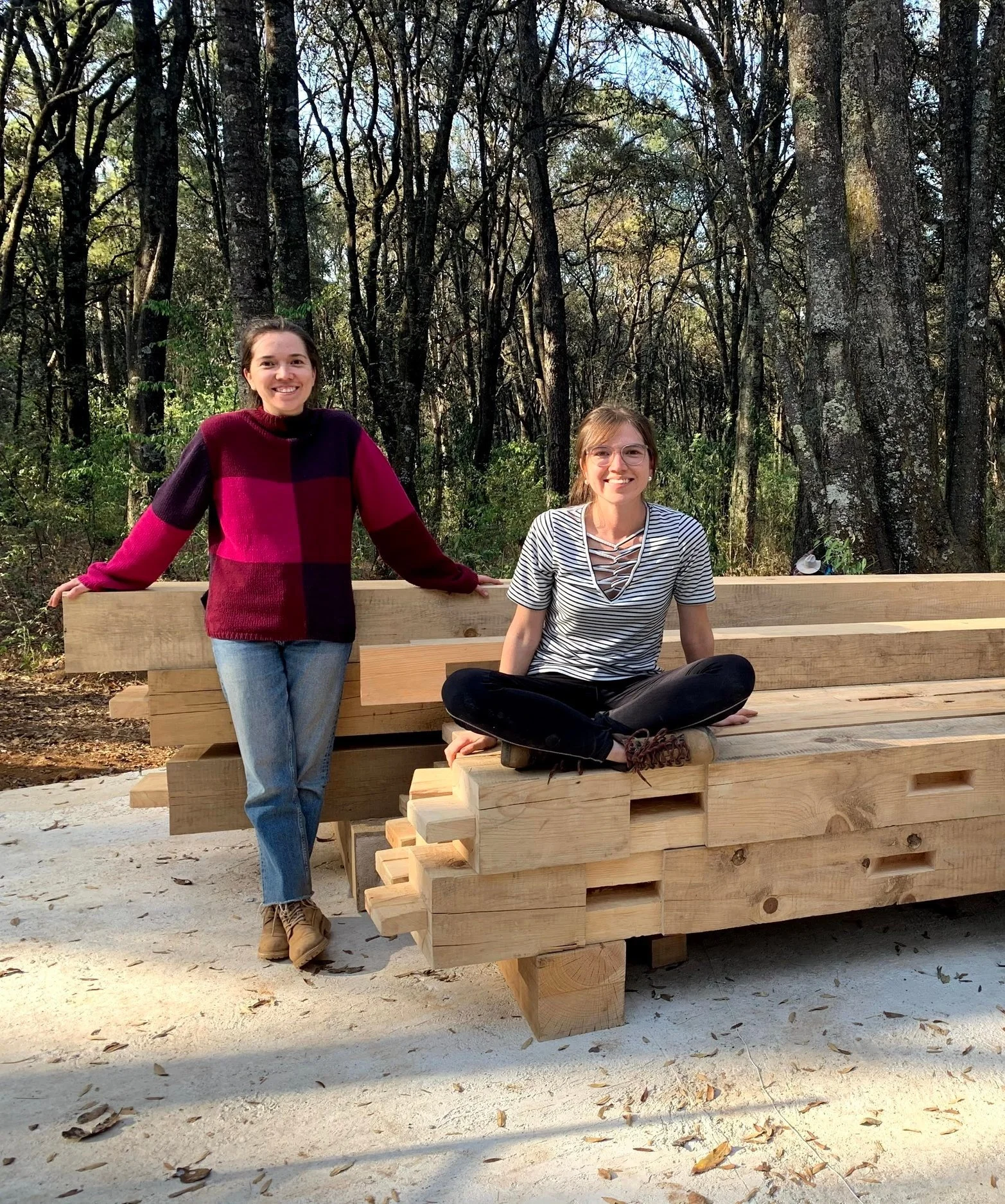 Las fundadoras del proyecto en un entorno de bosque, sobre estructuras de madera, explorando principios de bioconstrucción y arquitectura sustentable.