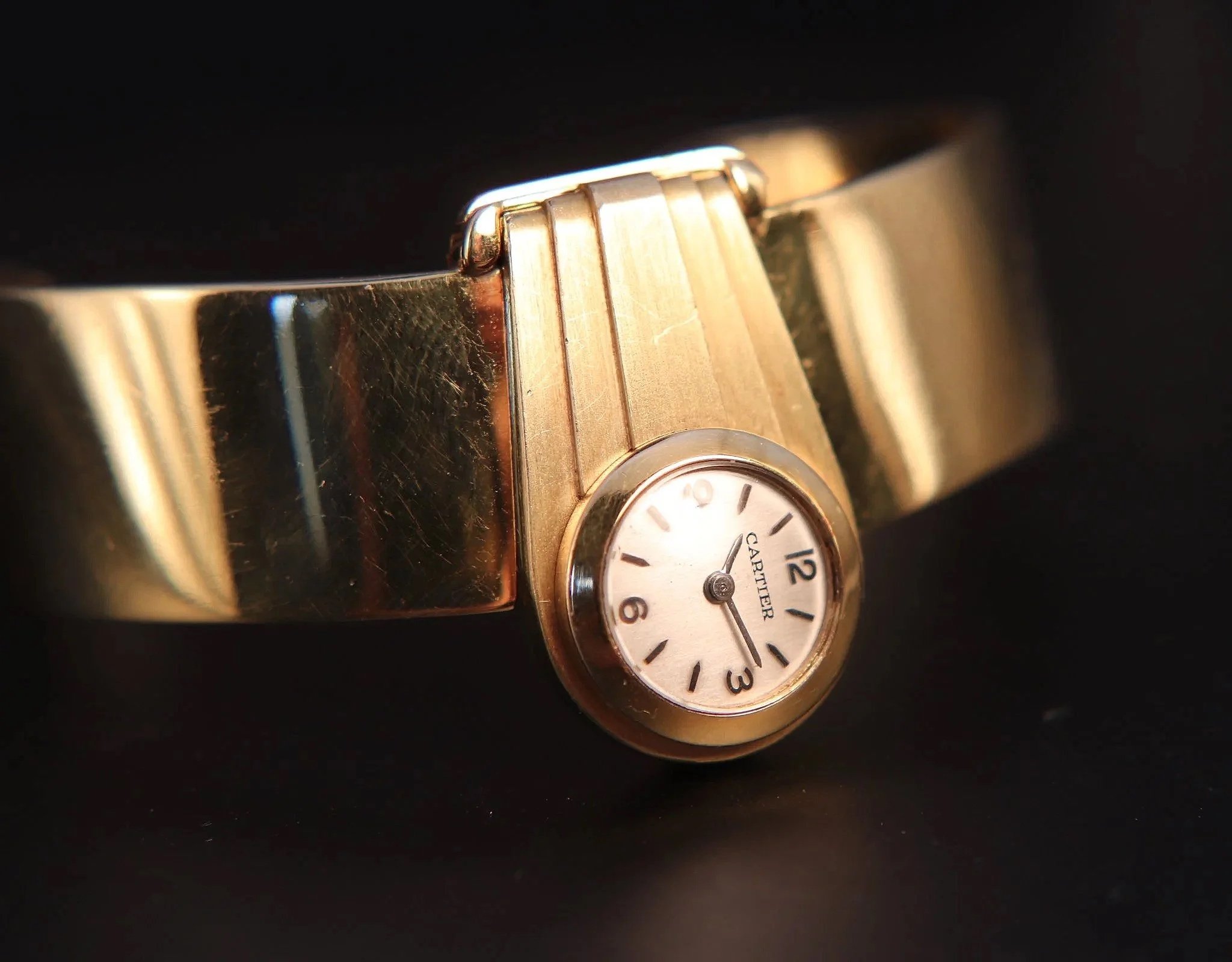 A gold Cartier wristwatch with a small round face and a metallic band, set against a black background.