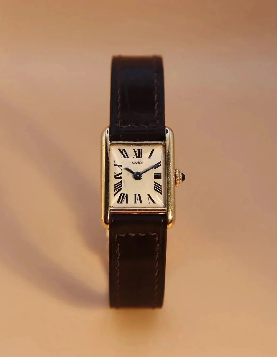 A rectangular gold wristwatch with a black leather strap and a white dial featuring Roman numeral hour markers.