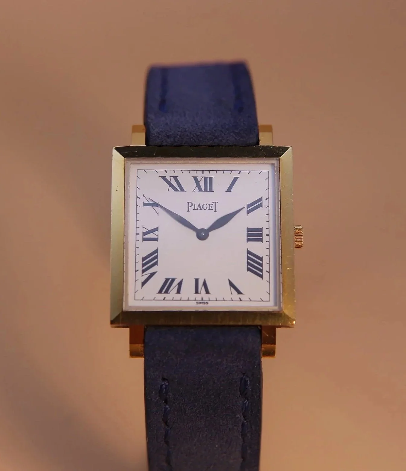 A rectangular gold wristwatch with a white dial, Roman numerals, and a dark leather strap. The watch shows the time as approximately 2:48.