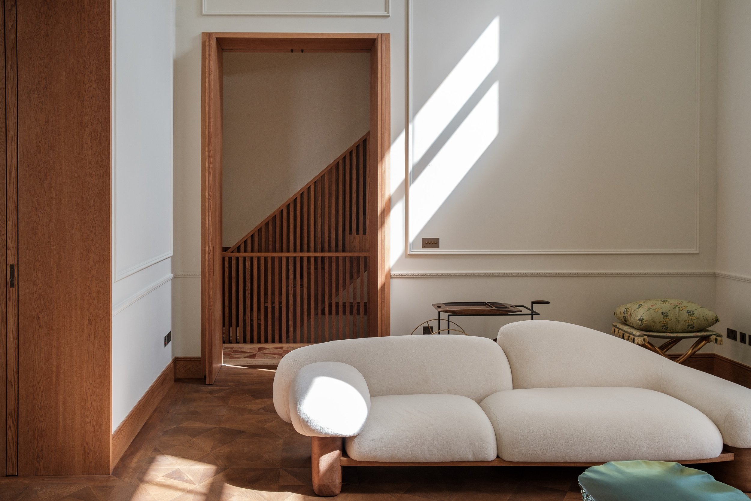 Modern living room with white plush sofa, wooden walls, and decorative slatted staircase entrance.