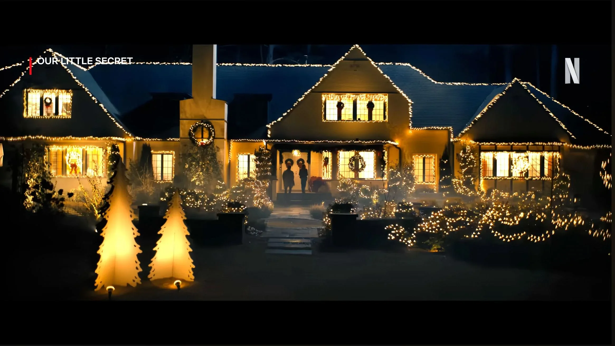 A large house decorated for Christmas with many lights, wreaths, and trees illuminated at night.