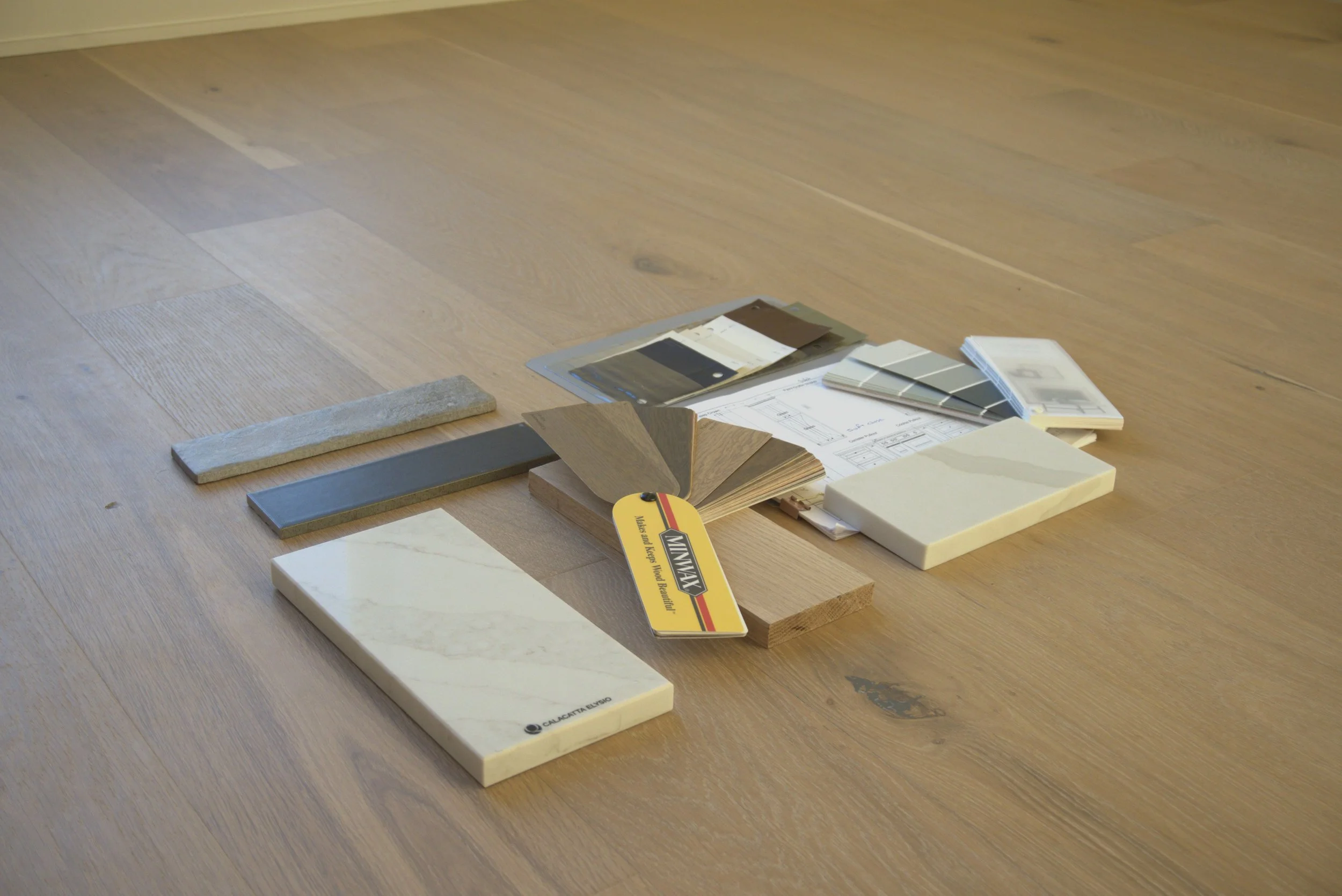Samples of various tiles, color swatches, and design plans laid out on a wooden floor for home renovation.