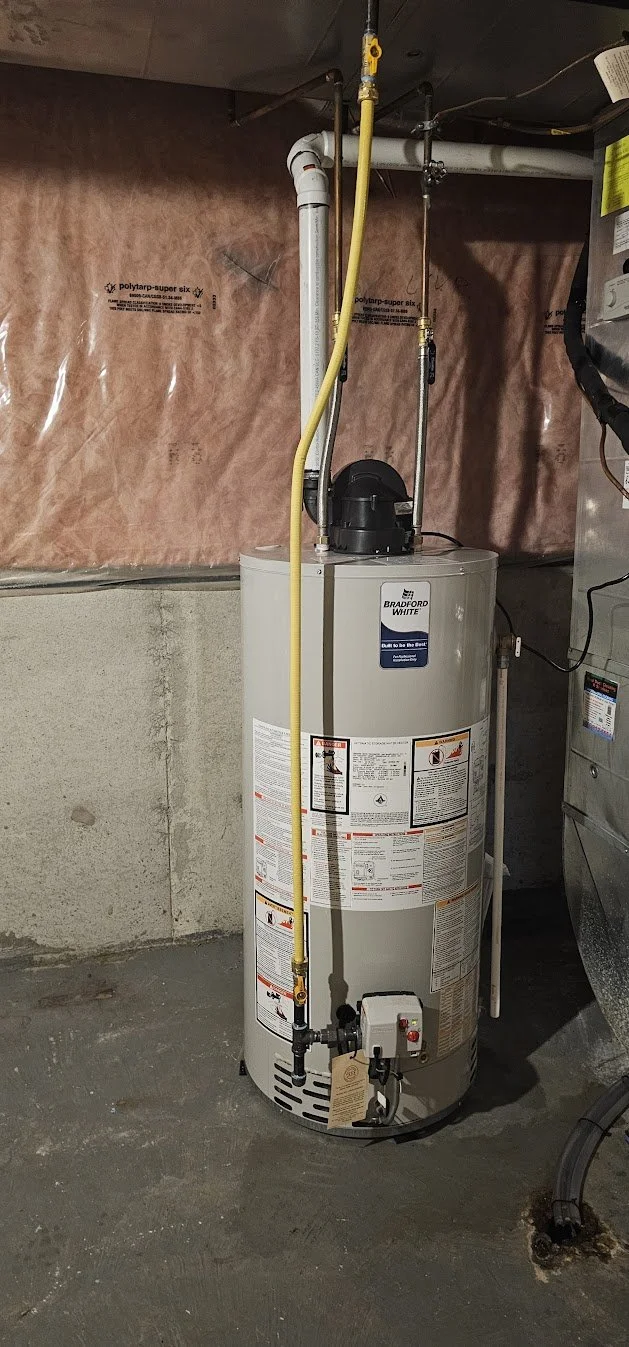 A Bradford White residential hot water heater in a basement with water pipes, gas valves, and electrical connections.
