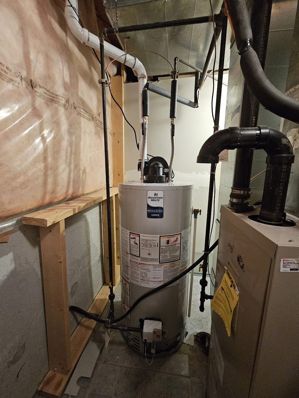 A water heater in a utility room, surrounded by plumbing pipes and connected to other heating and water system components.
