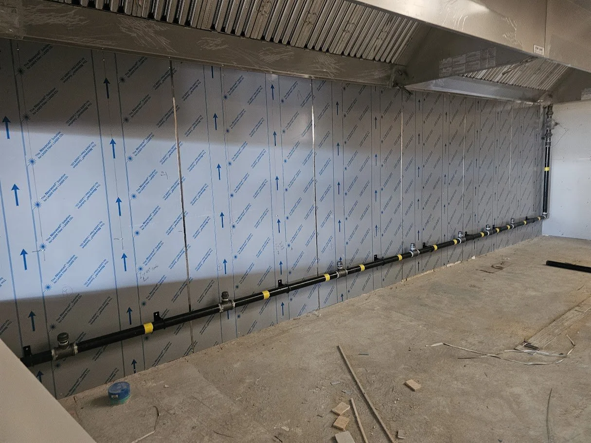 Underside of a construction area showing wall insulation, plumbing pipes, and construction debris.