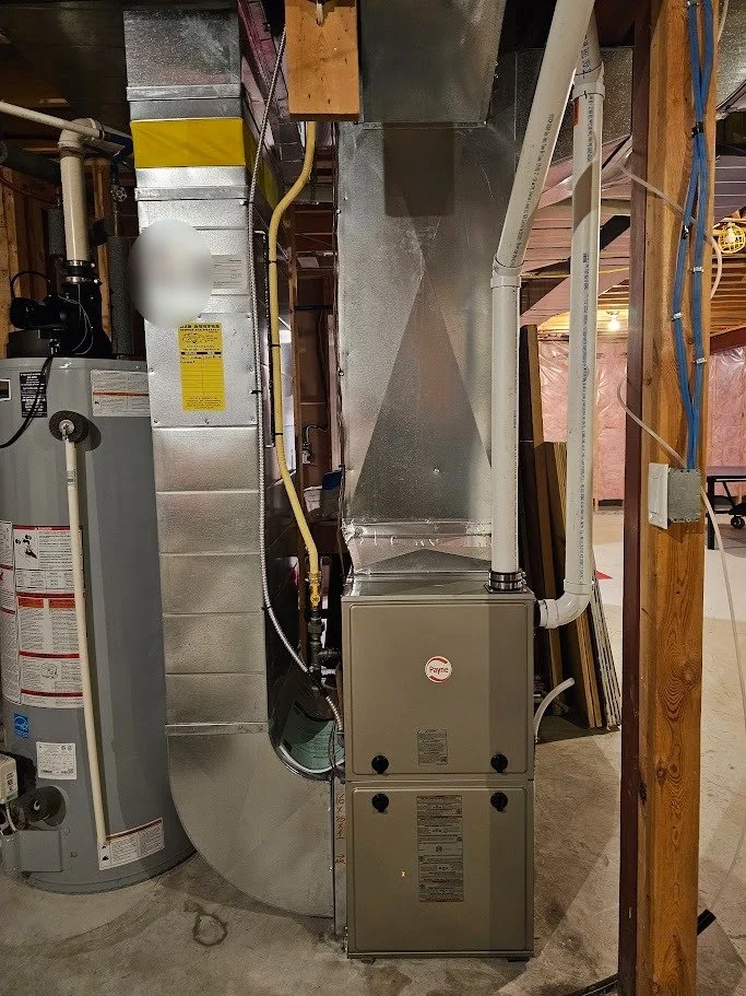 A furnace system with ductwork and pipes in a basement, next to a water heater.