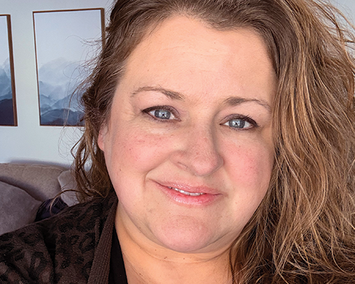 Close-up of a smiling woman with curly blonde hair and blue eyes.