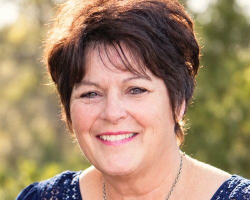 A woman with short dark hair smiling outdoors in natural light.
