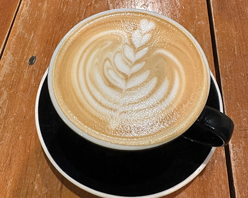 A latte with latte art in a black cup resting on a black saucer on a wooden table.