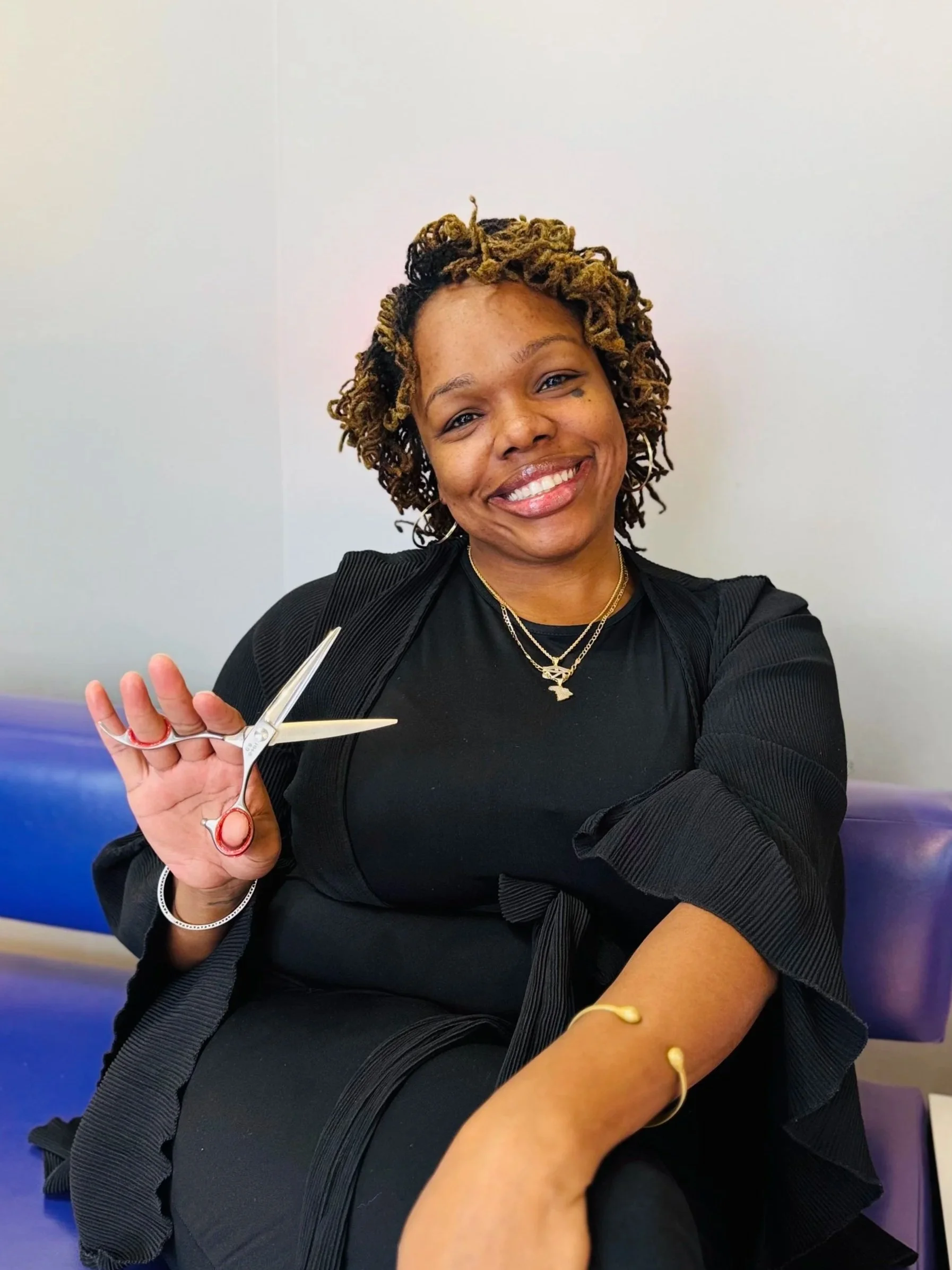 Woman sitting on a purple bench, smiling, holding a pair of scissors, with a bandage on her arm after donating blood.