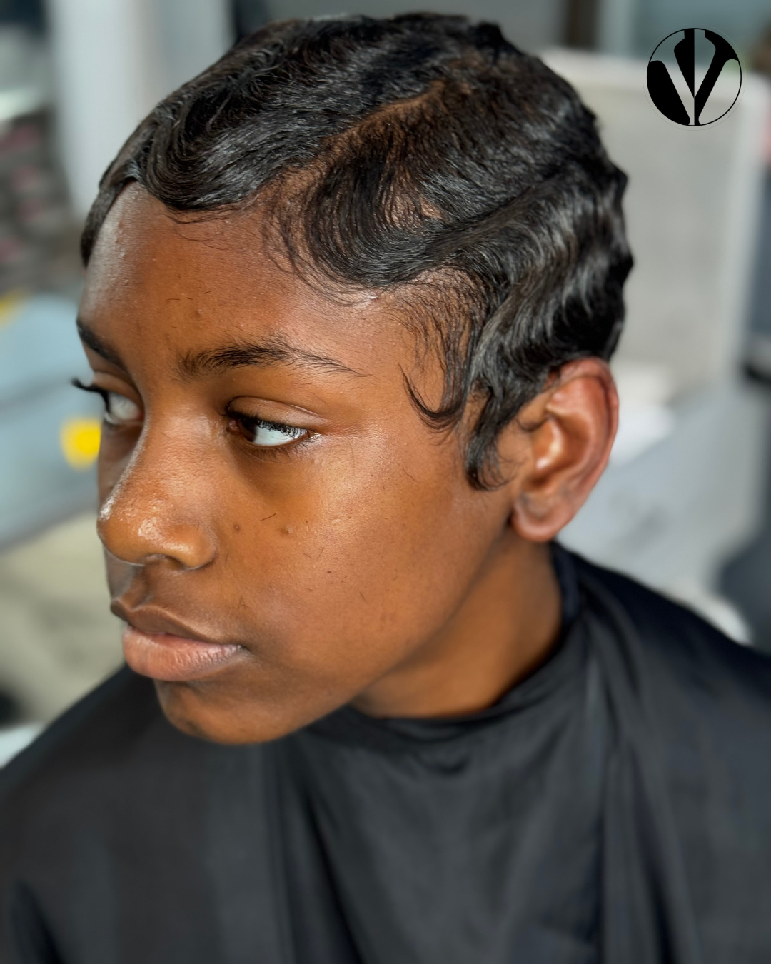 A person with short, wavy, black hair styled in finger waves, sitting in a salon chair.