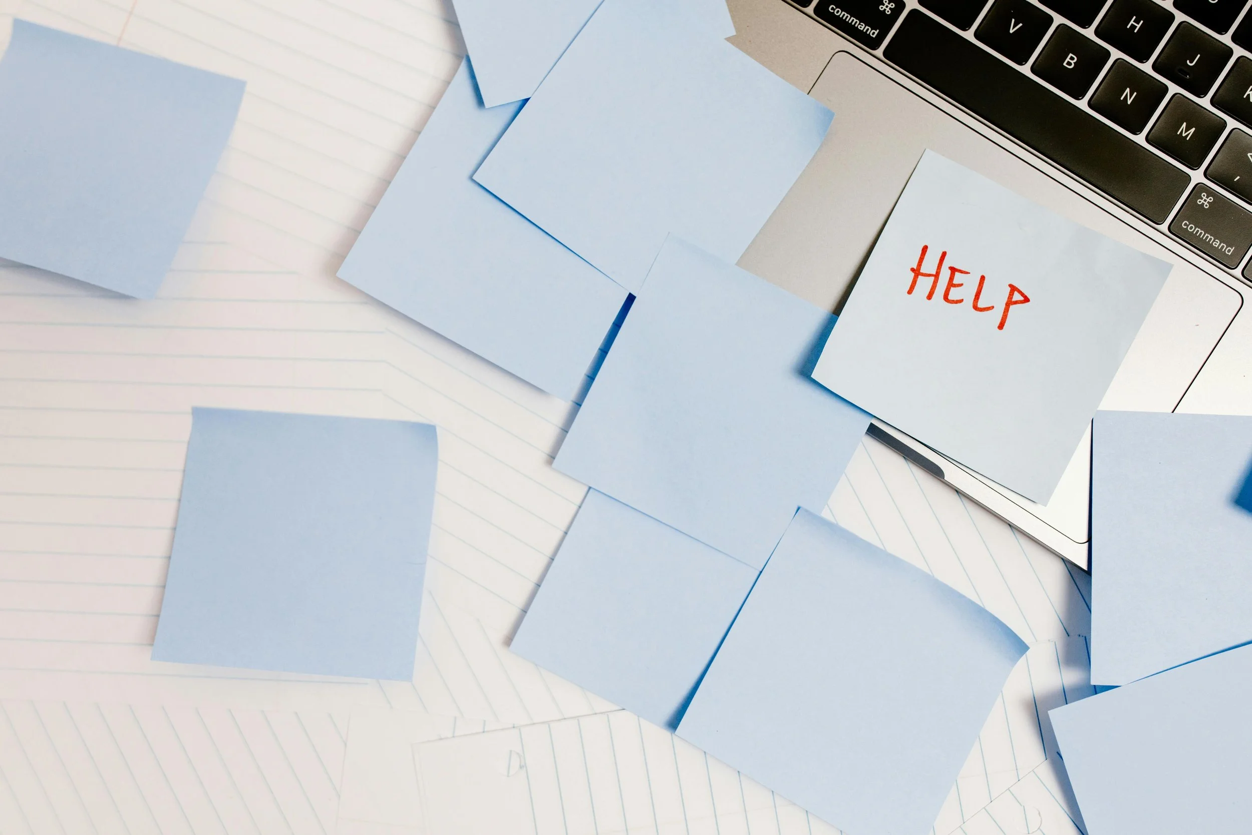Blauwe plakbriefjes op een laptop en papier, een met het woord 'HELP'.
