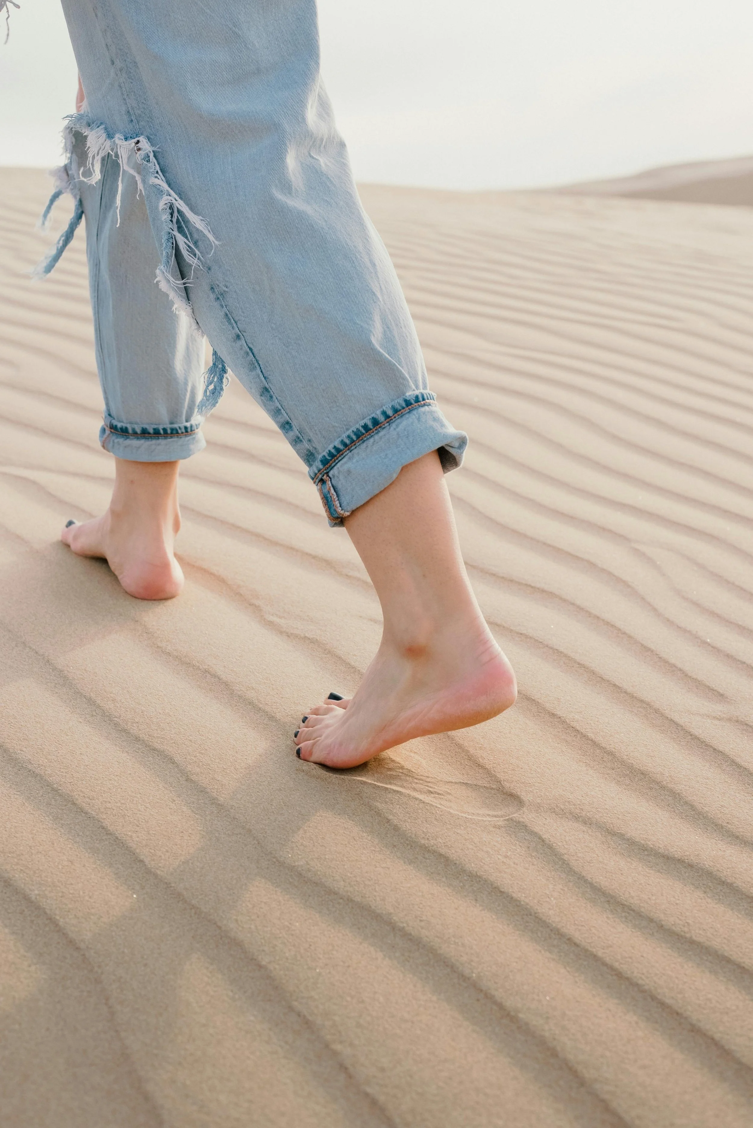 Blote voeten lopen over zandduinen, gekleed in opgerolde jeans.