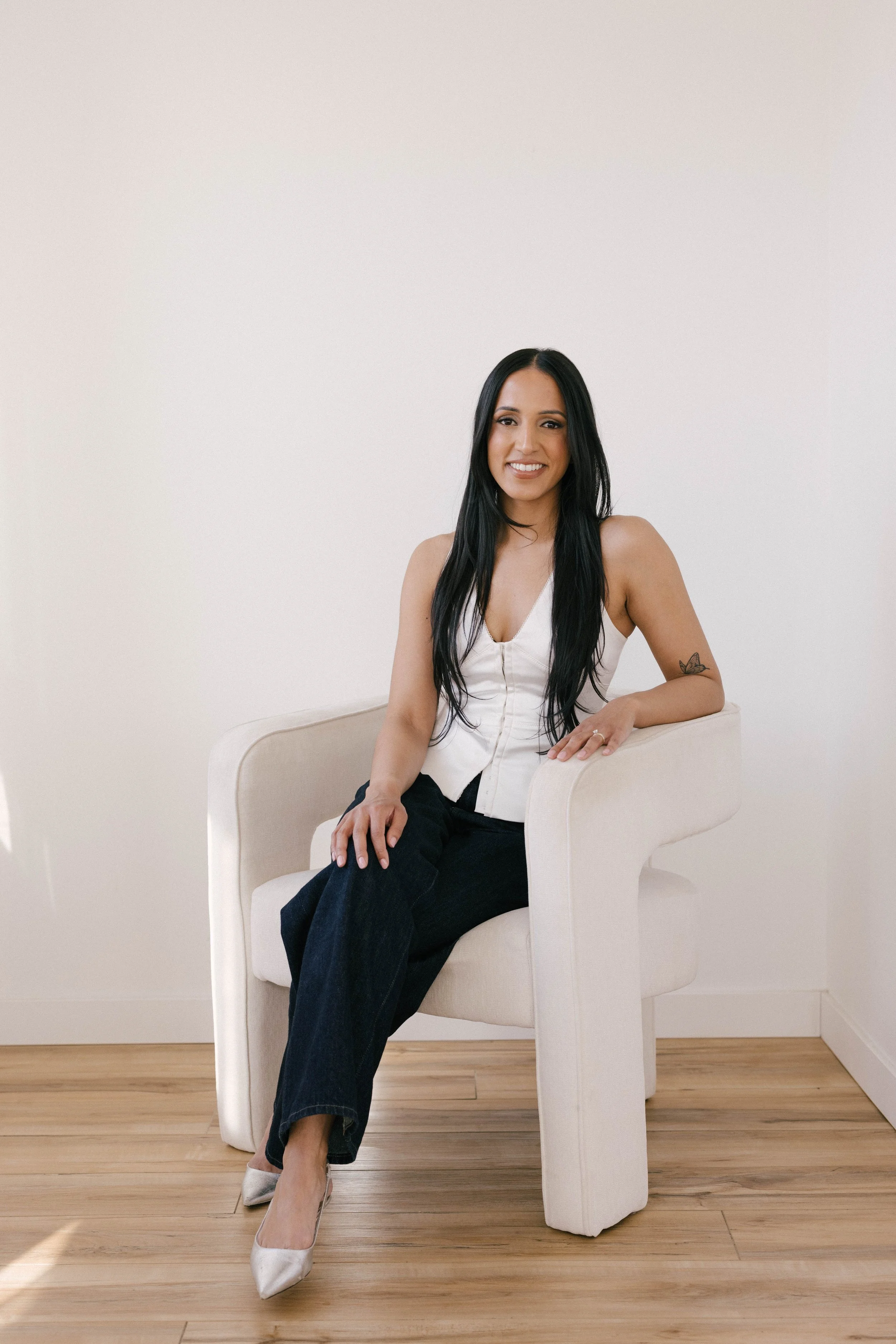 A woman with long black hair and a black blazer smiling, sitting in a well-lit room.