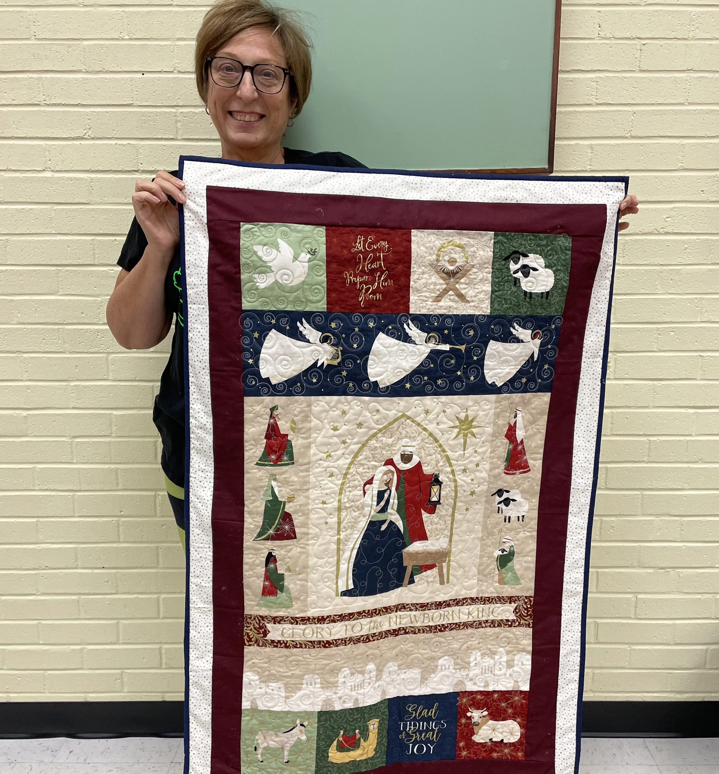 Person holding a quilt with Christmas-themed designs featuring angels, a nativity scene, and animals.