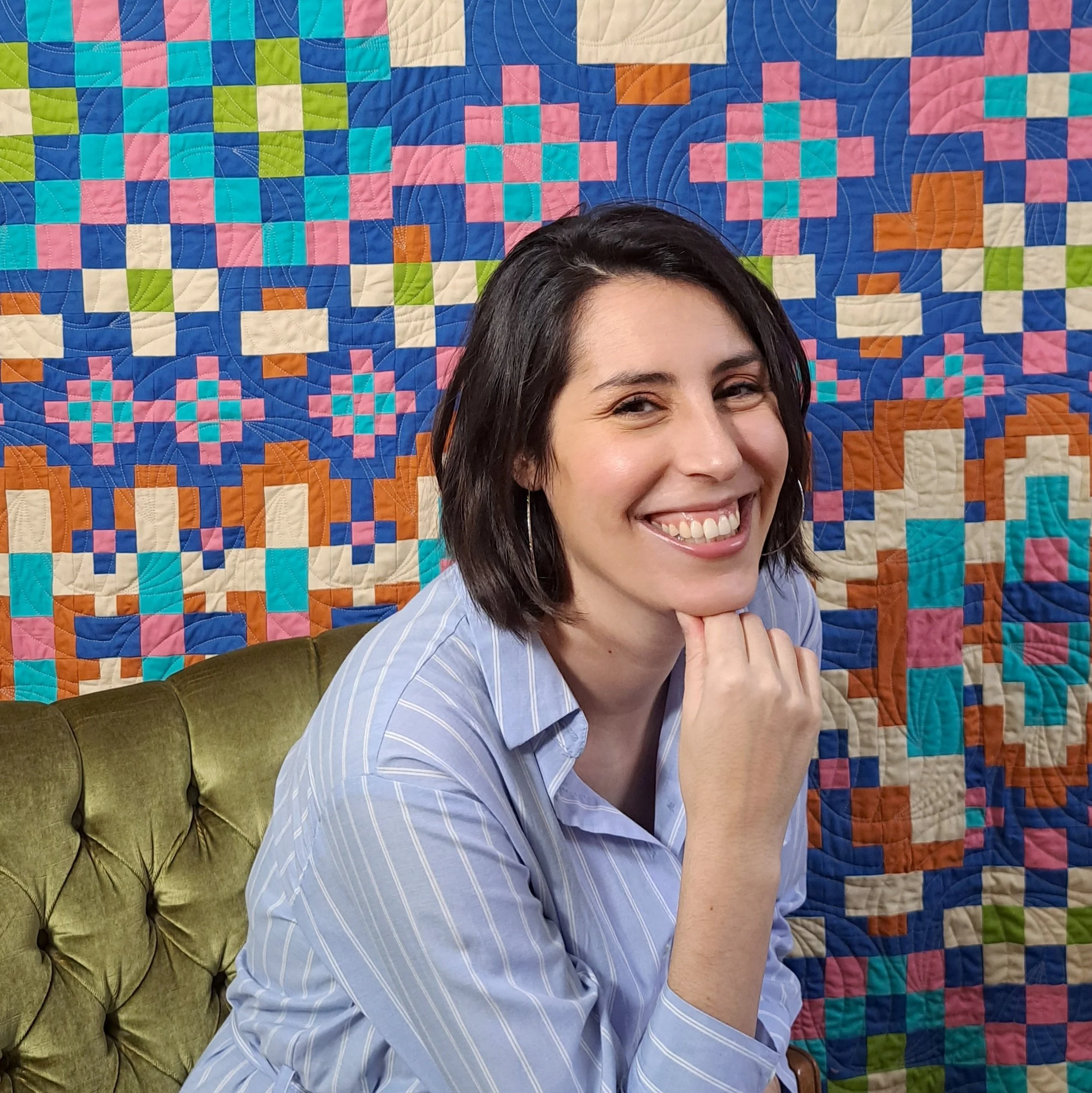 Smiling person sitting on a green couch in front of a colorful geometric quilt.
