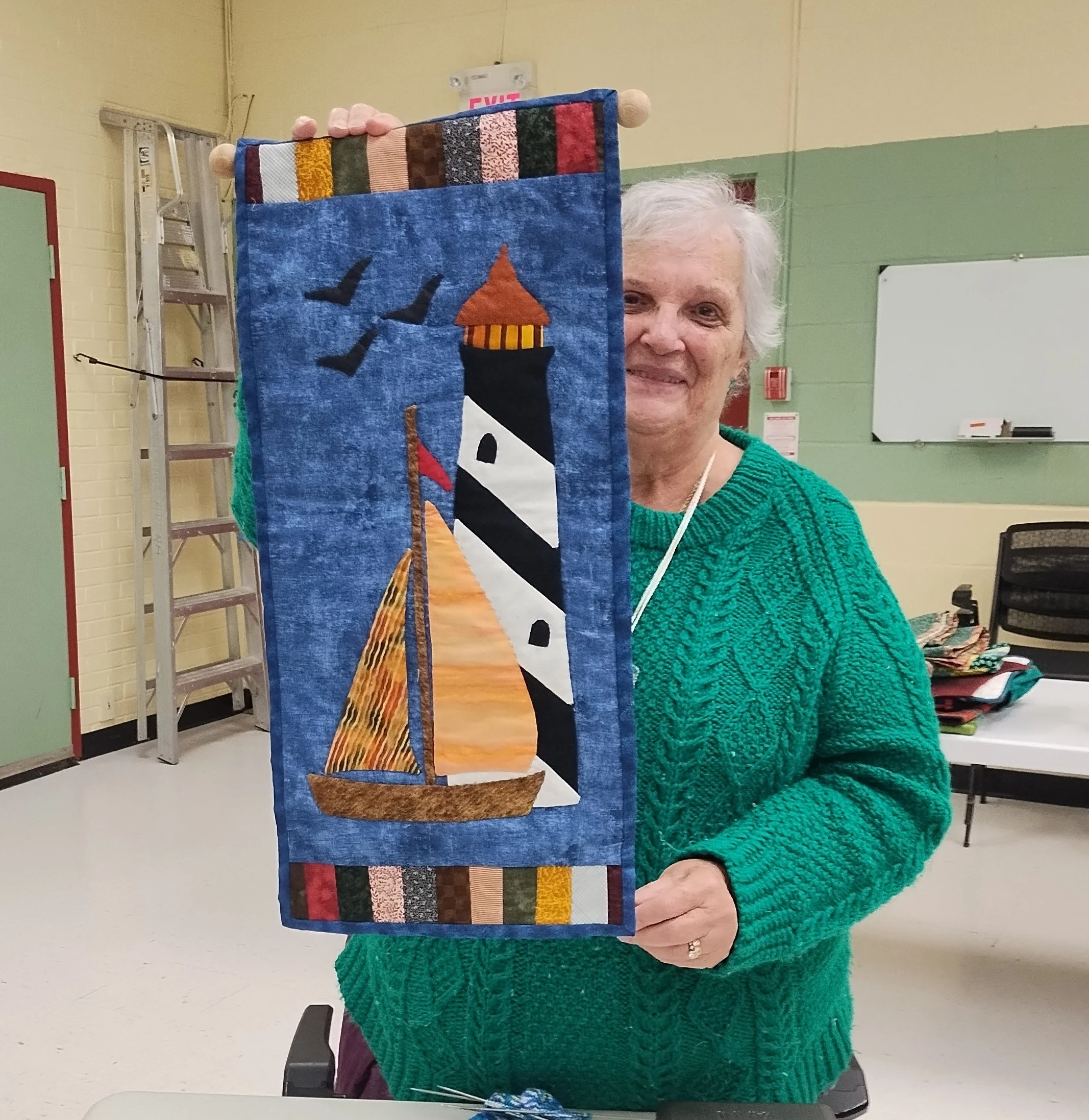 Woman holding a quilted wall hanging with a lighthouse and sailboat design.