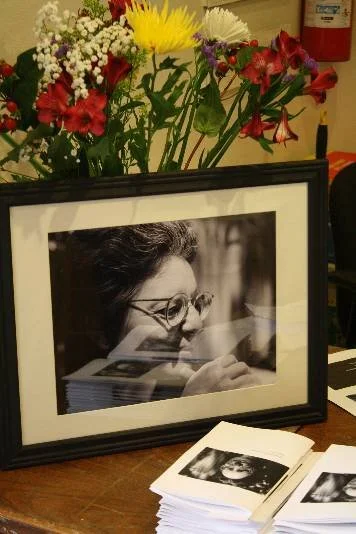 Photo of flowers, programs, and framed photo of Shulamith Fireston at memorial