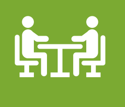 Icon of two people sitting at a table, facing each other, on a green background.