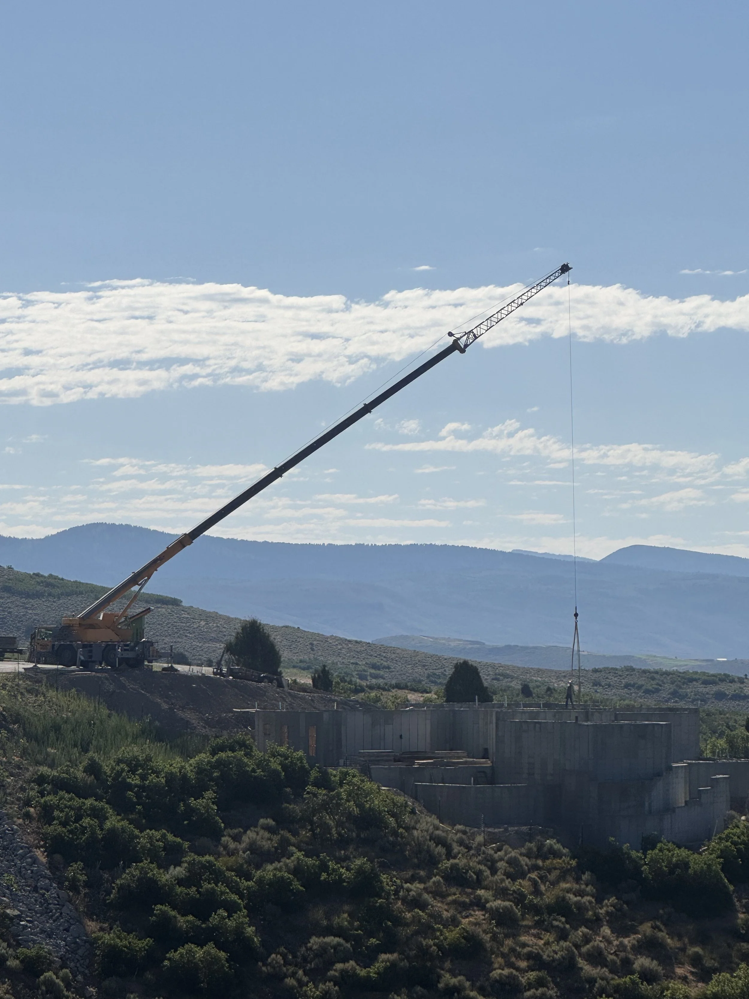 A construction crane on a hillside with mountains in the background and a partly cloudy sky.
