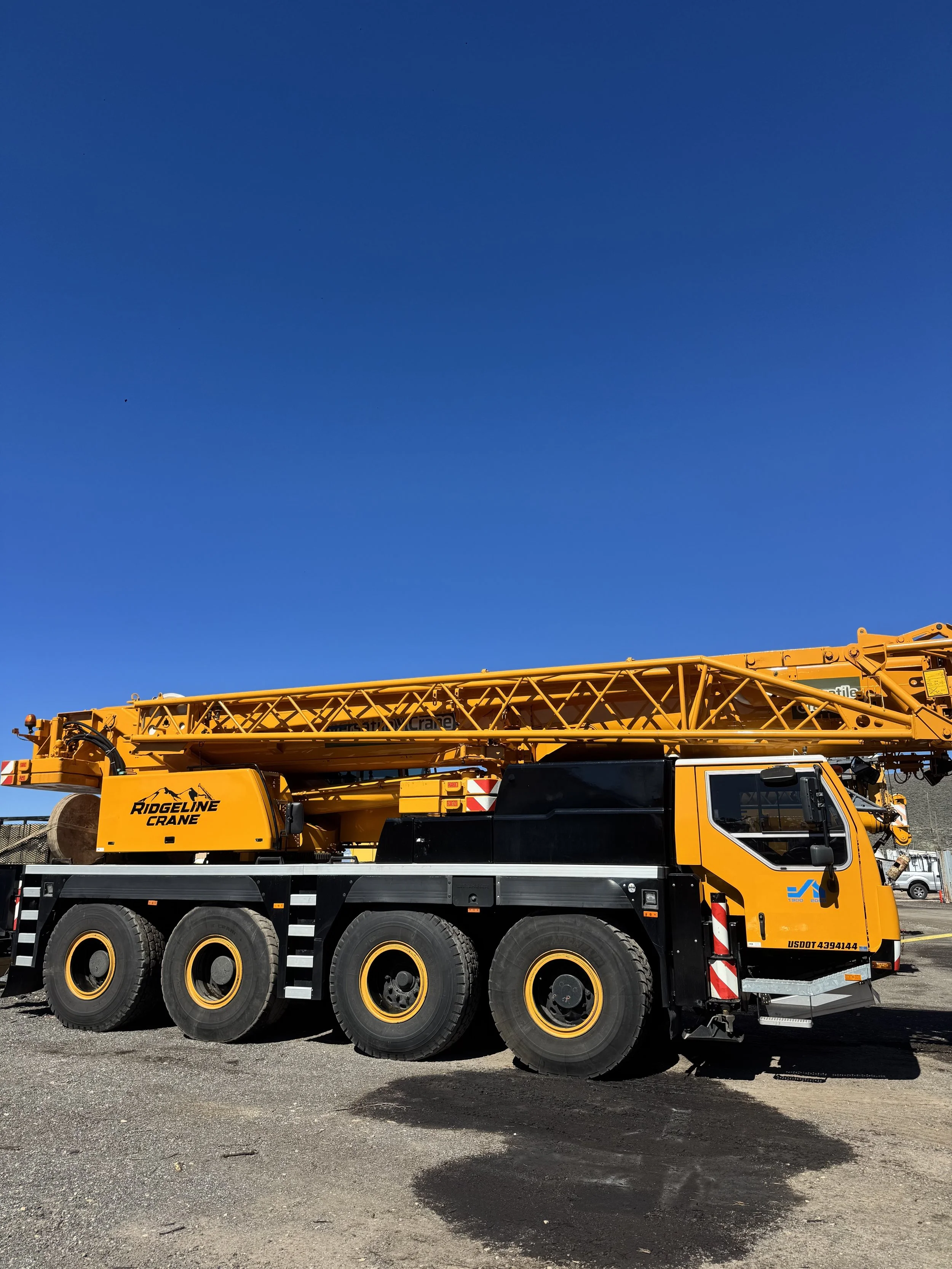 Yellow construction crane truck with black tires parked on a gravel surface under a clear blue sky.