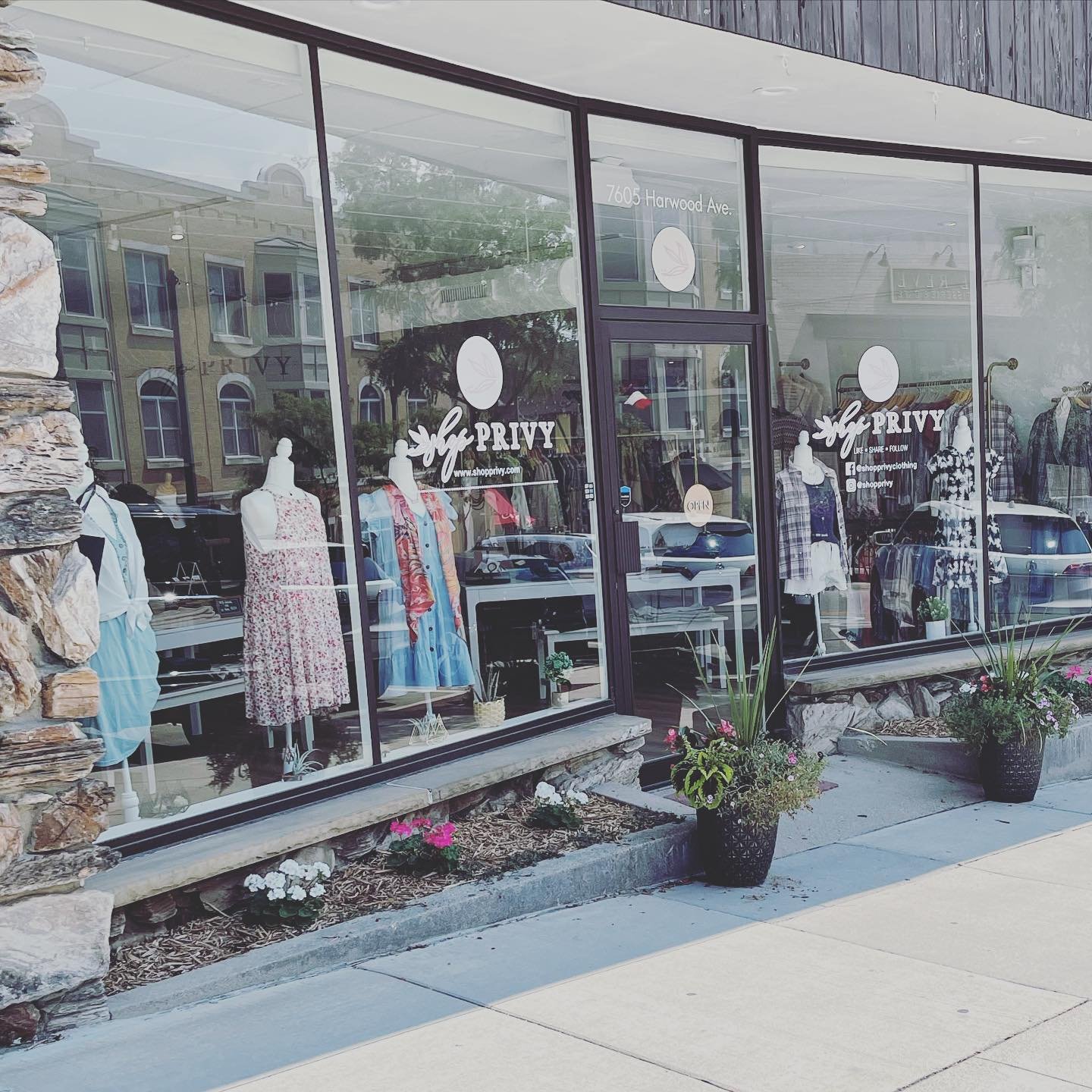 Storefront with large glass windows displaying mannequins dressed in casual clothing, with potted plants outside. The store sign reads 'PRIVY' and the address displayed is 7605 Harwood Ave.