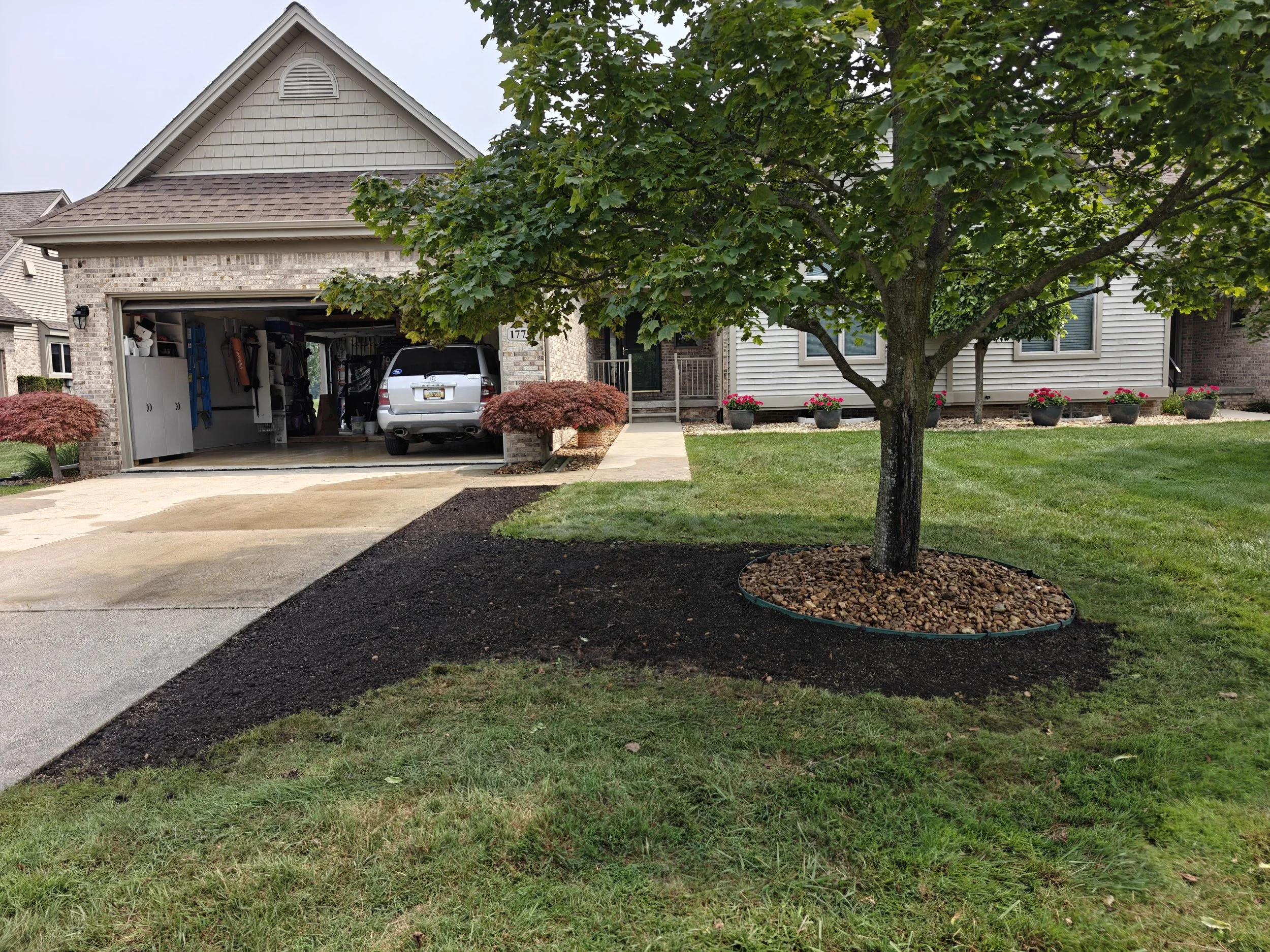 A house with a garage and a well-maintained front yard featuring a tree surrounded by mulch and a lush lawn.