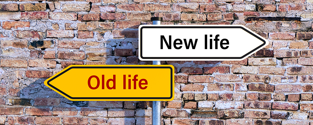 Signpost with arrows pointing to 'Old life' in yellow and 'New life' in white against a brick wall background.