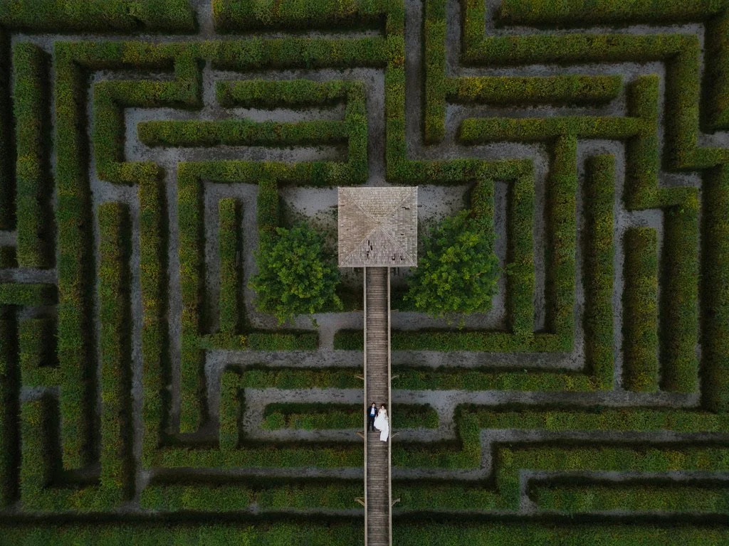 Vogelperspektive auf einen Irrgarten im Schoss Rosegg mit hohen Hecken, im Zentrum eine kleine Hütte mit einem Hochzeitpaar auf einer Brücke darunter.