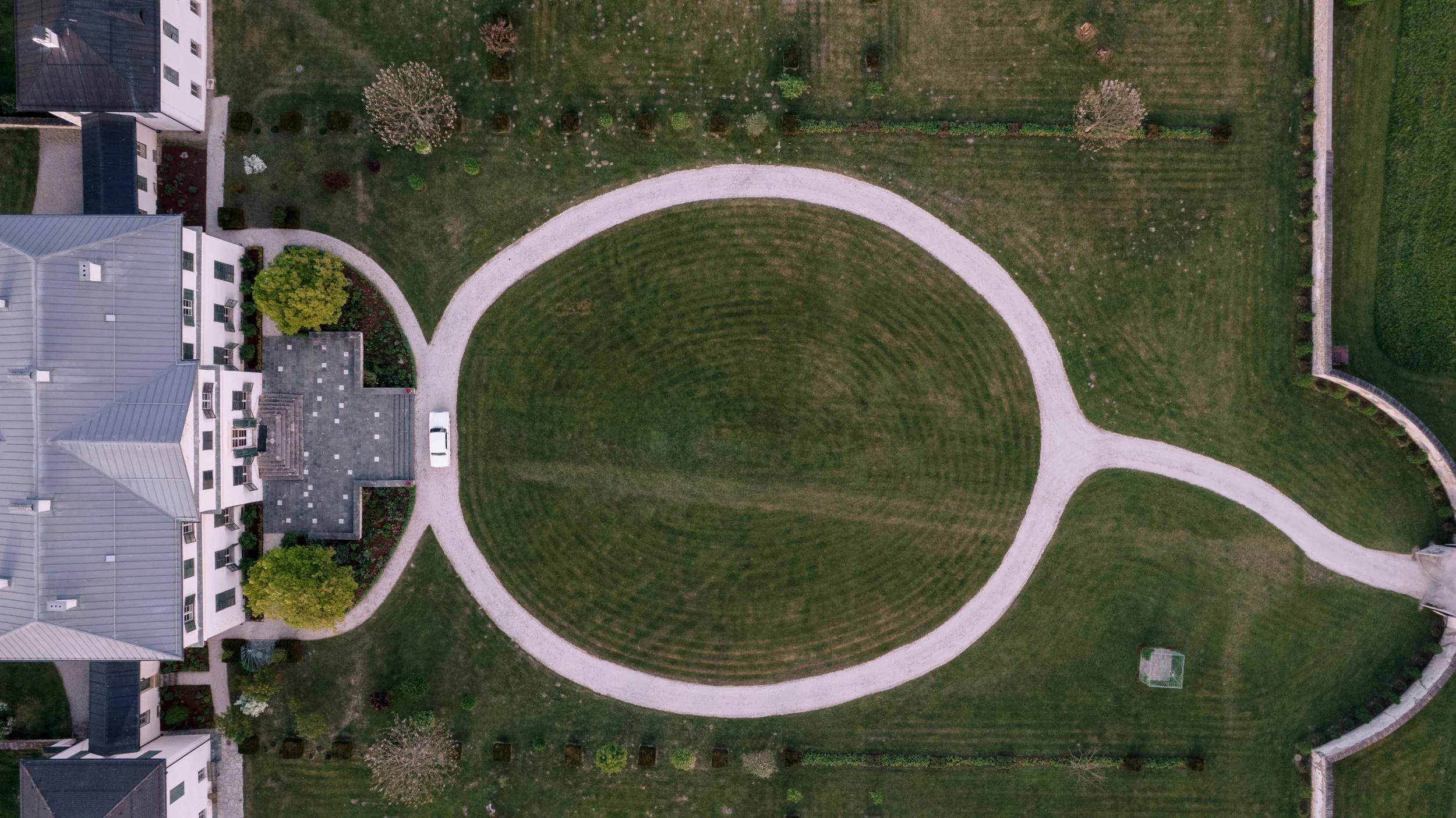 Luftaufnahme von Schloss Rosegg mit geometrischen Garten mit sanft geschwungenen Wegen, umgeben von Bäumen.